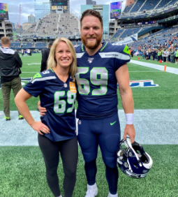 Ashley and Tyler Ott stand together on the field in a football stadium, both wearing jerseys with the number 69