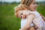 A young blonde mother carries her toddler daughter, who rests her head on her mother's shoulder